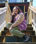 Leona is seated on a staircase wearing a purple jacket with gold trimmed Indian fabric.